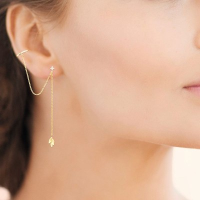 Boucles d'oreilles en plaqué or jaune 18 carats portées, avec chaîne fine, zircon solitaire et motif feuillage.